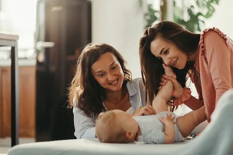 Close up of LGBTQ+ couple with two mothers playing with newborn baby