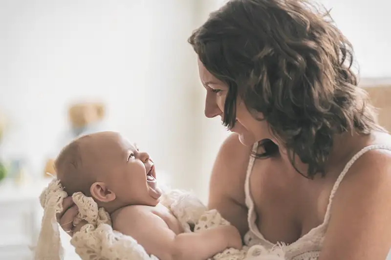 A close up side shot of a mom holding her newborn IVF baby who is smiling and looks happy