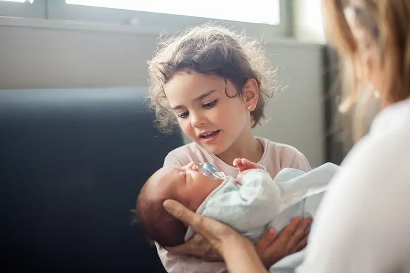 Young little girl is holding her sibling for the first time, conceived via IVF