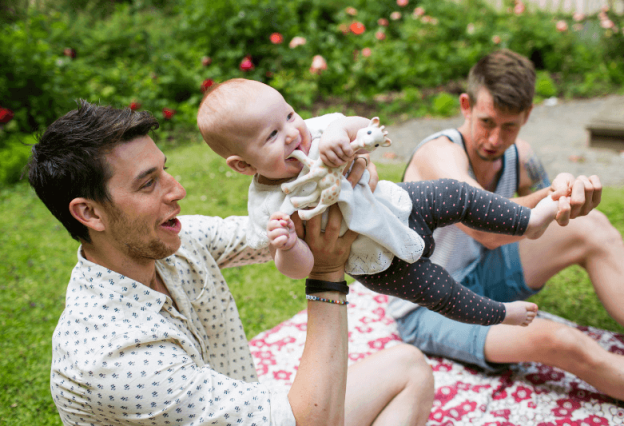 Male same-sex couple play with their baby in the park