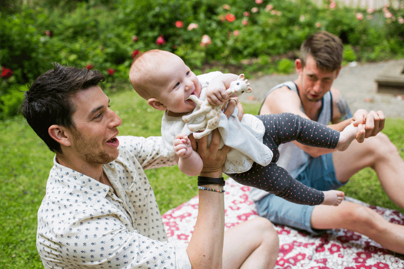 Male same-sex couple play with their baby in the park