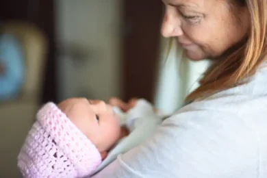 Woman smiling holding new born baby wearing a knitted pink hat